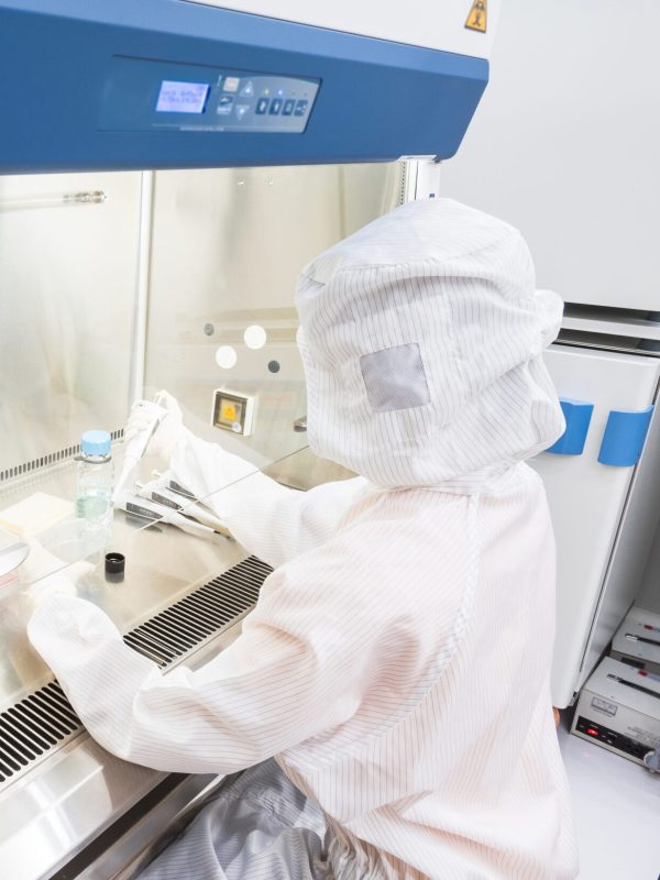 A scientist in sterile coverall gown pipetting medium or reagents for cell culture experiment in biological safety cabinet. Doing biological research in clean environmental. Cleanroom facility